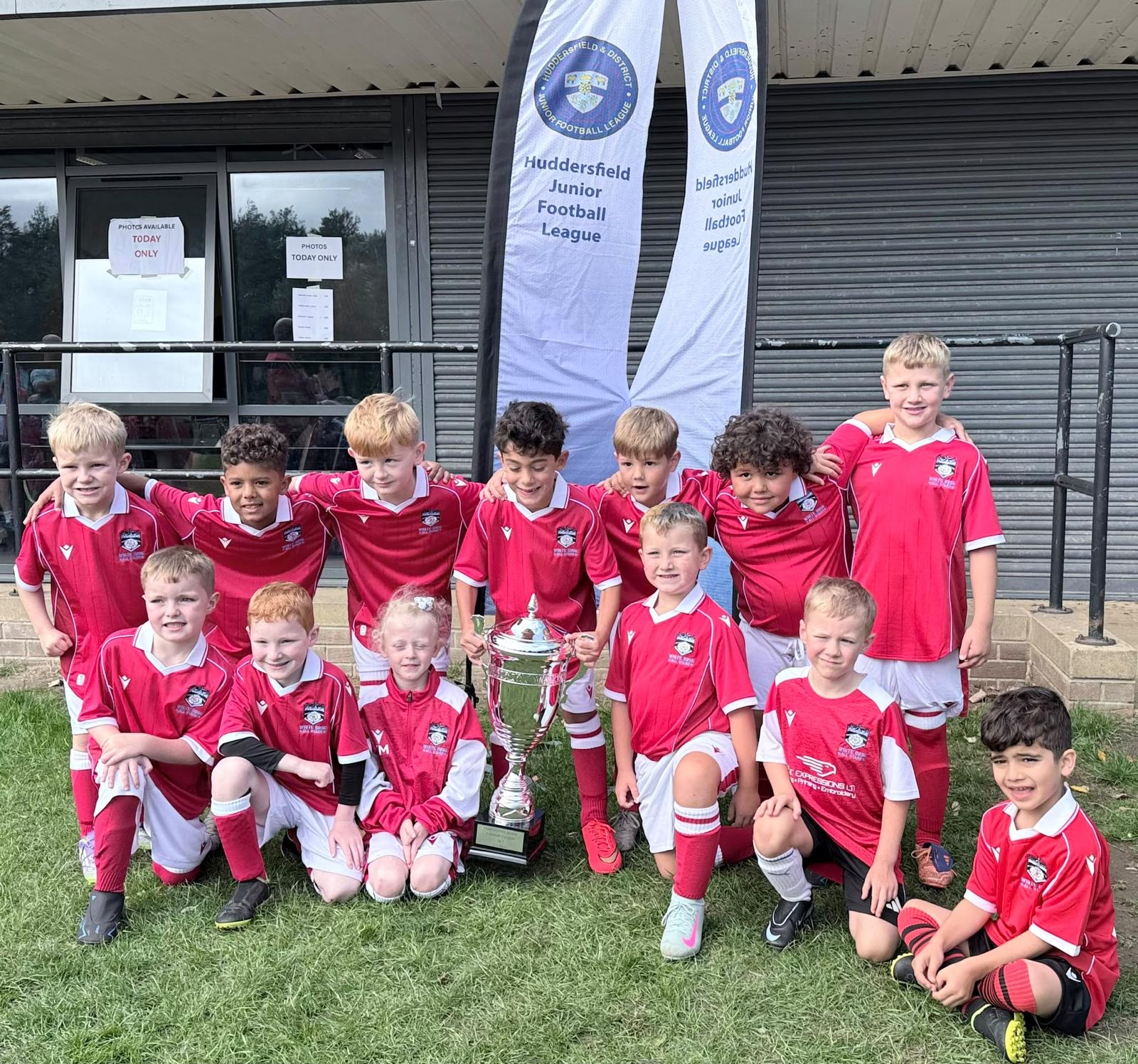 Young White Rose players in red kits celebrating with a silver trophy