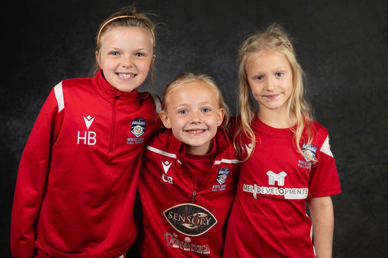 Three smiling girls in White Rose kit